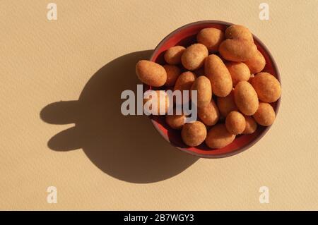 A small bowl with orange nuts with shadows like rabbits on the light yellow background. Trendy conceptual minimalistic photo for Easter Holiday 2020 Stock Photo