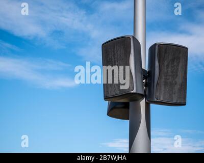 Black speakers suspended from a metal pole with blue sky as a background. Outdoor speakers for music . Stock Photo