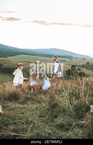 Positive happy family running in country field in summer time. Happy young family, father, mother and two children enjoying the summer in mountains Stock Photo