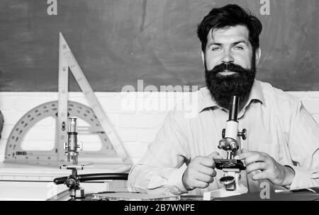 Fascinating research. Set up microscope. Teacher sit desk with microscope. Man bearded hipster classroom chalkboard background busy with biological observation. School teacher looking microscope. Stock Photo