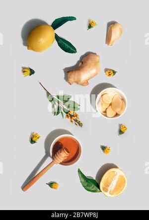 Lemon whole and cut out piece, ginger, honey and yellow flowers pattern on light grey background. Flat lay, top view. Immunity, vitamins, natural health concept Stock Photo