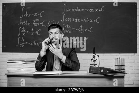 Calling parents. School teacher call mobile phone while sit classroom chalkboard background. Teacher bearded man talk mobile phone. Call colleague ask advice. Pedagogue keep in touch with colleagues. Stock Photo