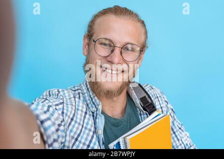 Happy man student blogger take selfie on blue background, phone camera view. Stock Photo
