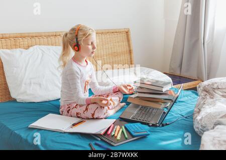 Caucasian girl child meditating in bed and learning online on laptop Internet. Virtual class lesson on video during self isolation at home. Distant re Stock Photo