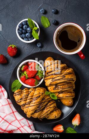 Croissant with fresh berries and cup of coffee on black.