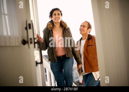 Smiling mid adult couple walking through the front door of a home. Stock Photo