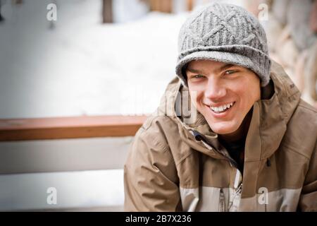 Portrait of a smiling young man wearing a knitted hat outdoors in the snow. Stock Photo