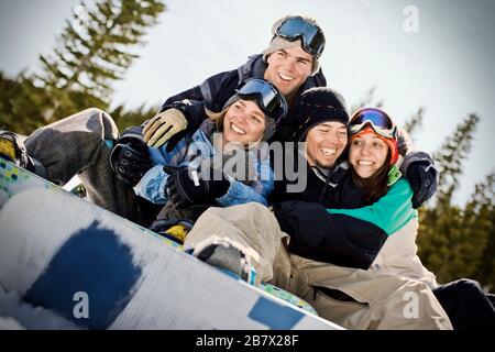 Two smiling young couples wearing snow gear and sitting with arms around each other outdoors. Stock Photo