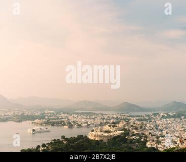 Elevated view of lake Pichola flanked by City Palace, Lake Palace, and Aravallli hills at sunrise in summer in Udaipur, Rajasthan, India. Stock Photo