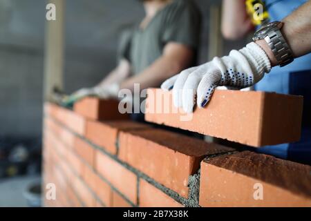 Two workers making red brick wall at construction site Stock Photo