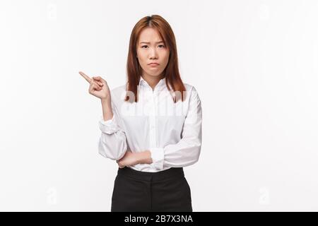 Portrait of upset and distressed asian female entrepreneur, sulking disappointed pointing finger left at something bad, feel let down and disturbed Stock Photo