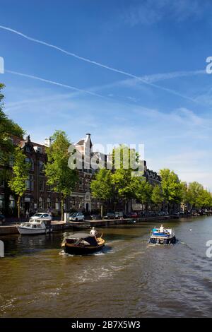 View of people riding small boats on canal doing a cruise tour. Trees, clear blue sky and historical, traditional buildings are also in the view. It i Stock Photo