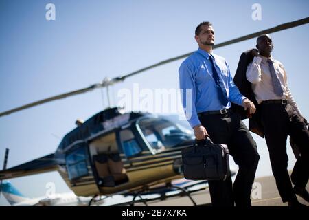 Two mid-adult businessmen leaving a helicopter at an airport. Stock Photo
