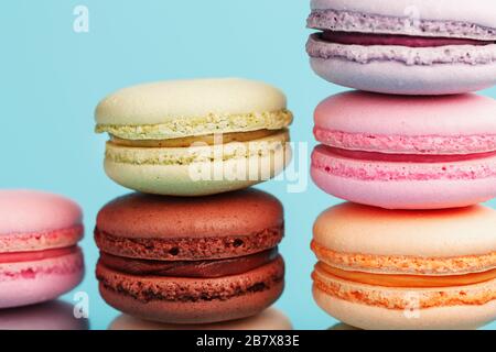 Macaroni cookies of different colors are arranged in the shape of pyramid steps on a blue background. Stock Photo