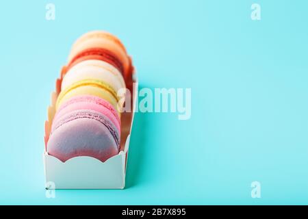 Macaroni cookies of different colors in a white box on a blue background. Free space, close-up shooting from above. The concept of minimalism Stock Photo
