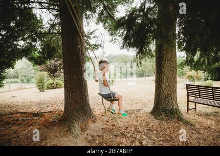 Side view of boy on swing under tree against trees Stock Photo