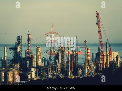 a clustered view of an oil refinery with boats in the background Stock Photo