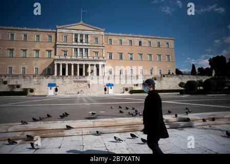 Athens, Greece. 18th Mar, 2020. A man, wearing protective mask, walks in front of the empty of people main Syntagma square in Athens, Greece. The Greek government gave instructions to citizens to stay at home to prevent the spread of the Covid-19 coronavirus disease. ©Elias Verdi/Alamy Live News Stock Photo