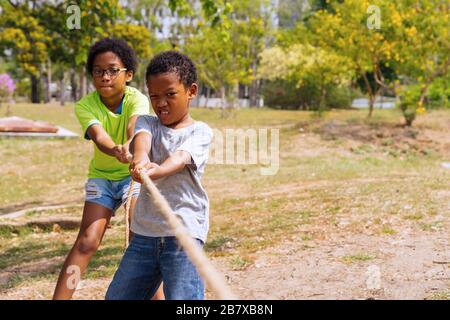 African American boy and girl pull rope together in tug of war competition - brother and sister on leisure activity - strength and teamwork concept Stock Photo