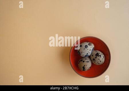 A small bowl with three quail eggs on the light yellow background. Trendy conceptual minimalistic photo for Easter Holiday 2020 Stock Photo