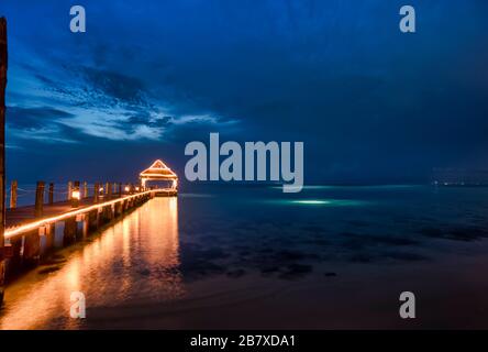 Wooden pier illuminated at night with blue sky background, and reflections on the Caribbean sea in the island of Cozumel Mexico Stock Photo
