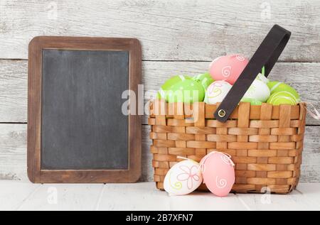 Easter greeting card with colorful easter eggs basket in front of wooden wall. With chalkboard for your greetings Stock Photo