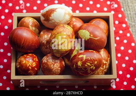 Chicken eggs colored with old-fashioned natural method by onion husks. Brown eggs with different natural patterns in box on red. Selective focus with Stock Photo