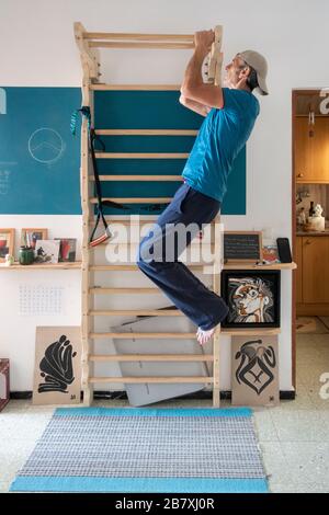 61 year old man exercising at home on homemade wall bars in small apartment.