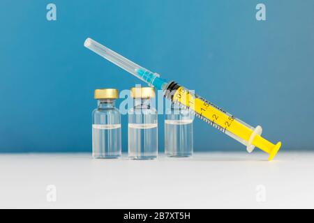 Glass vials with liquid and empty syringe on blue background. Coronavirus vaccine. nCov-2019 disease. Illness prevention. Medical injection. Flu shot Stock Photo