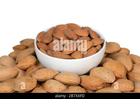 Peeled almonds in a white bowl surrounded by raw almonds in shell. Isolated on white background. Stock Photo