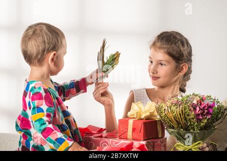 Little cute boy gives a bouquet to his charming older sister on International Women's Day. Concept of women's holidays and gifts Stock Photo