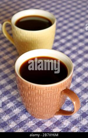Vertical Image of Two Cups of Hot Black Coffee on Purple Check Pattern Tablecloth Stock Photo