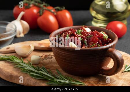 Sun-dried tomatoes with garlic, rosemary and spices in a clay bowl on an olive wood cutting board. Stock Photo