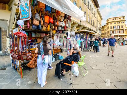 A female tourist buys souvenirs from a small shop stand selling leather goods and clothing in Piazza Santa Croce in Florence Italy Stock Photo