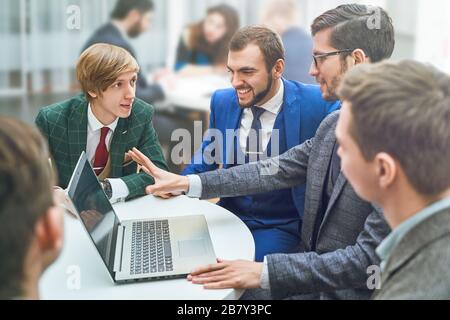 Group of young business people working and communicating while sitting at the office desk together with colleagues sitting in the background Stock Photo
