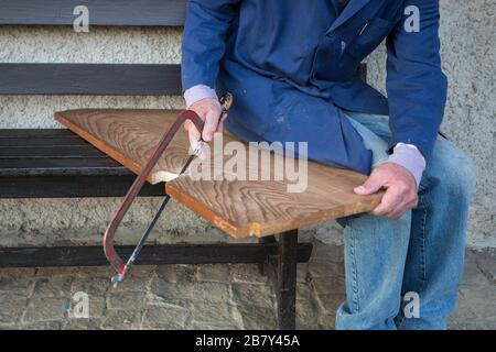 hands of older man working cutting plank with wood handsaw outside on the ground on picnic Stock Photo