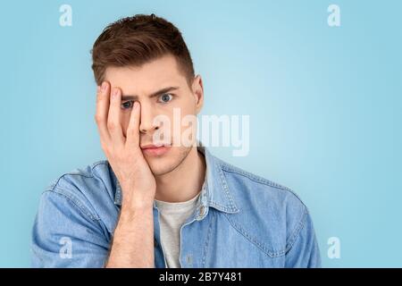 Young adult guy with shocked face holding hand near cheek Stock Photo