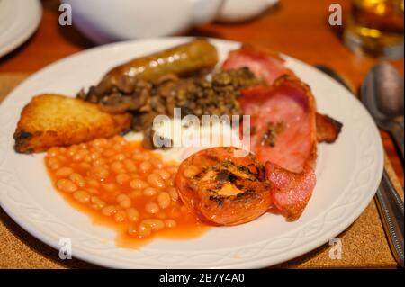 White board with full Scottish breakfast with bacon, fried egg, beans, tomato, roasted sausage, pudding, hash browns and haggis Stock Photo