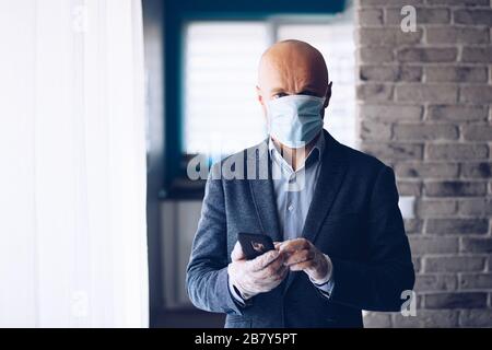 Businessman wearing protective medical mask and using smartphone at home. Stock Photo