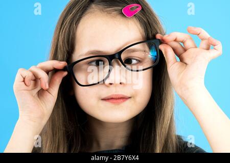 Close up portrait of a cross eyed child school girl wearing looking glasses isolated on blue background. Stock Photo