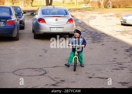 POZNAN, POLAND - Mar 08, 2020: Happy small Caucasian Polish boy riding a running bike on asphalt with parked cars. Stock Photo