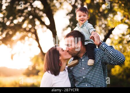 Parents kissing while cute baby boy is on dad's shoulders Stock Photo