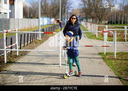 POZNAN, POLAND - Mar 08, 2020: Adult woman and child riding a scooter on a footpath with barrier at the Rataje park. Stock Photo