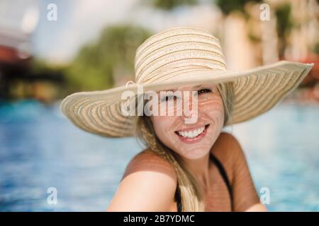 smiling Young woman sun bathing in tropical pool with sun hat Stock Photo