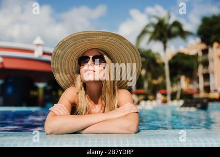 Young woman sun bathing in tropical pool with sun hat Stock Photo