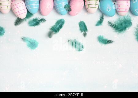 Easter concept. Pastel colored eggs and feathers on light background with space for text. Top view, flat lay. Stock Photo