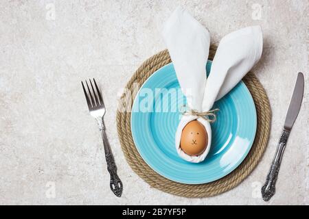 Easter table setting with egg in napkin like Easter Bunny and cutlery. Holidays background, top view. Stock Photo