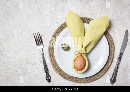 Easter table setting with egg in napkin like Easter Bunny and cutlery. Holidays background, top view. Stock Photo