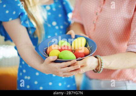 Closeup on mother and daughter showing a blue plate with colorful easter eggs at home in sunny spring day. Stock Photo