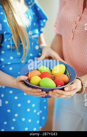 Closeup on mother and child showing a blue plate with colorful easter eggs in the living room in sunny spring day. Stock Photo